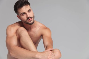 oturan çıplak adam tarafına gri arka plan üzerinde görünüyor.