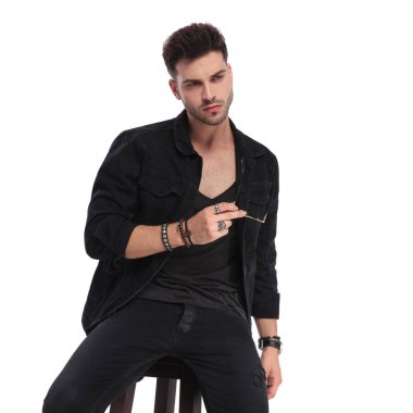 Casual adam güneş gözlüğü tutarak ve beyaz arka tarafa bakıyor siyah giysili oturmuş