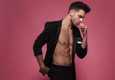 dalgın adamla çıplak göğüs tarafına geri alınan bir siyah smokin giyiyor ve kırmızı arka plan üzerinde ayakta iken aşağı görünüyor