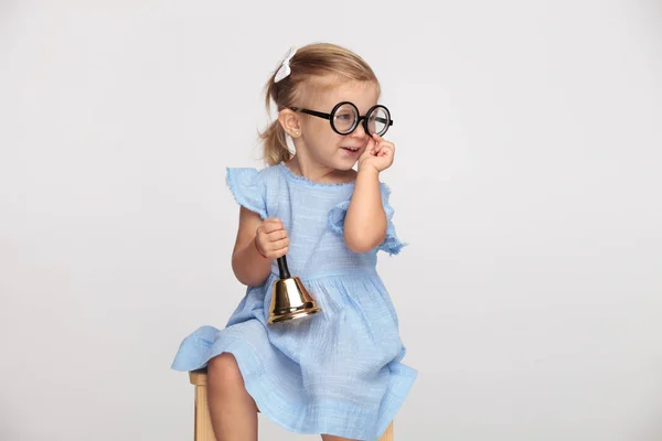 微笑的小美丽的女孩戴着眼镜 抱着铃铛看着灰色背景的一面 — 图库照片