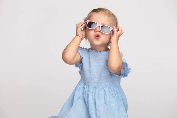 Linda Niña Fijando Sus Gafas Sol Sobre Fondo Gris —  Fotos de Stock