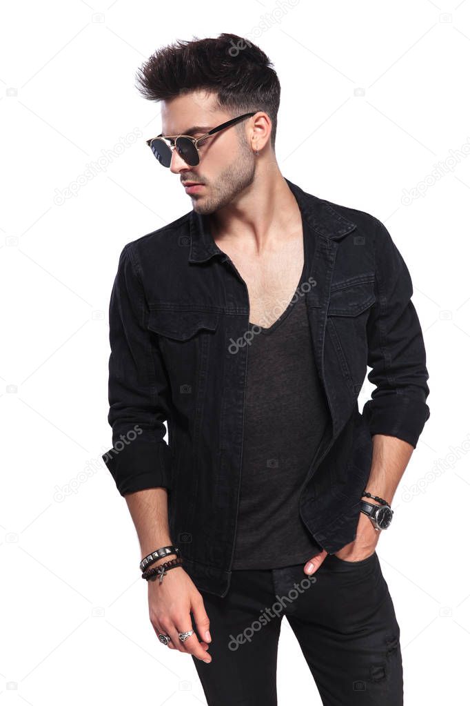 portrait of attractive casual man in black clothes looking down to side while standing on white background