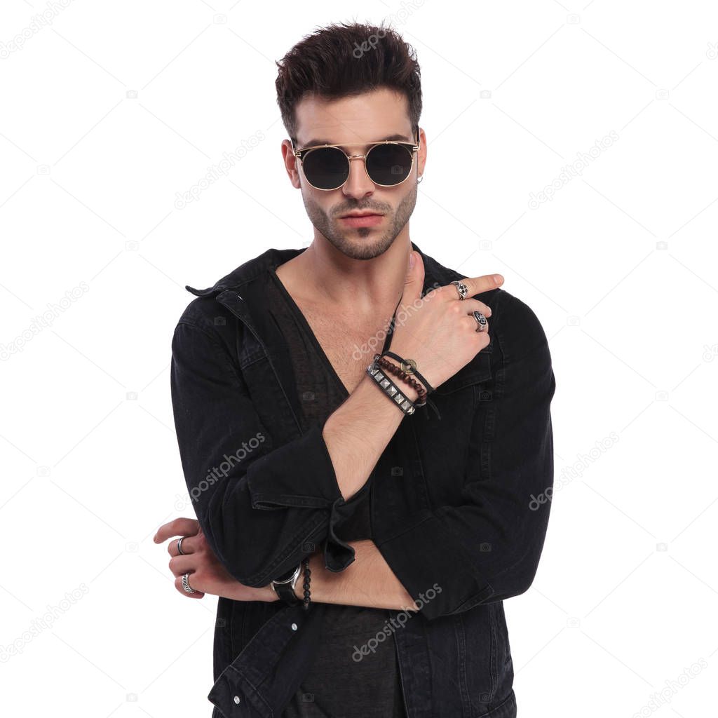 portrait of sexy man wearing a black shirt showing his bracelets and rings while standing on white background
