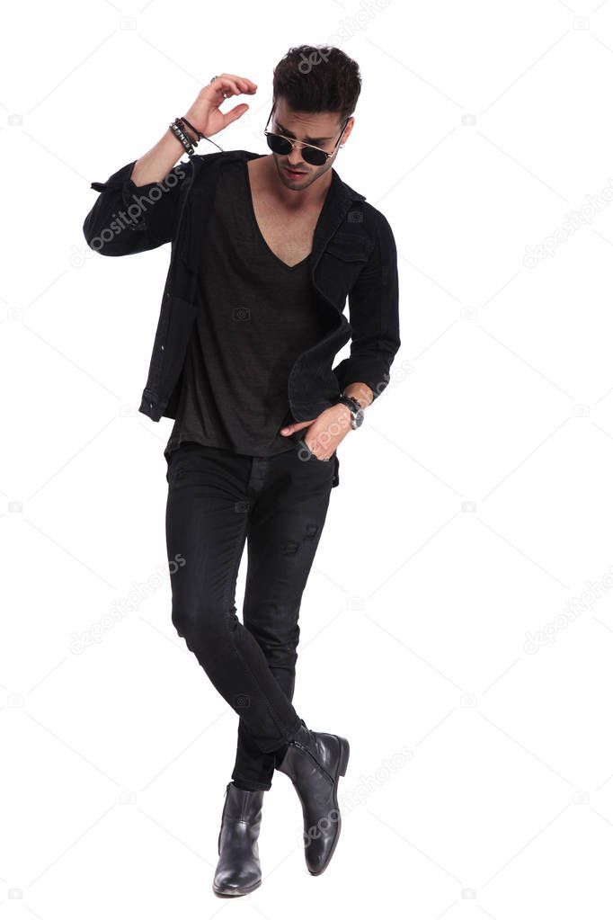 relaxed man in black clothes standing on white background with legs crossed and looking down while having a hand in the air, full length picture