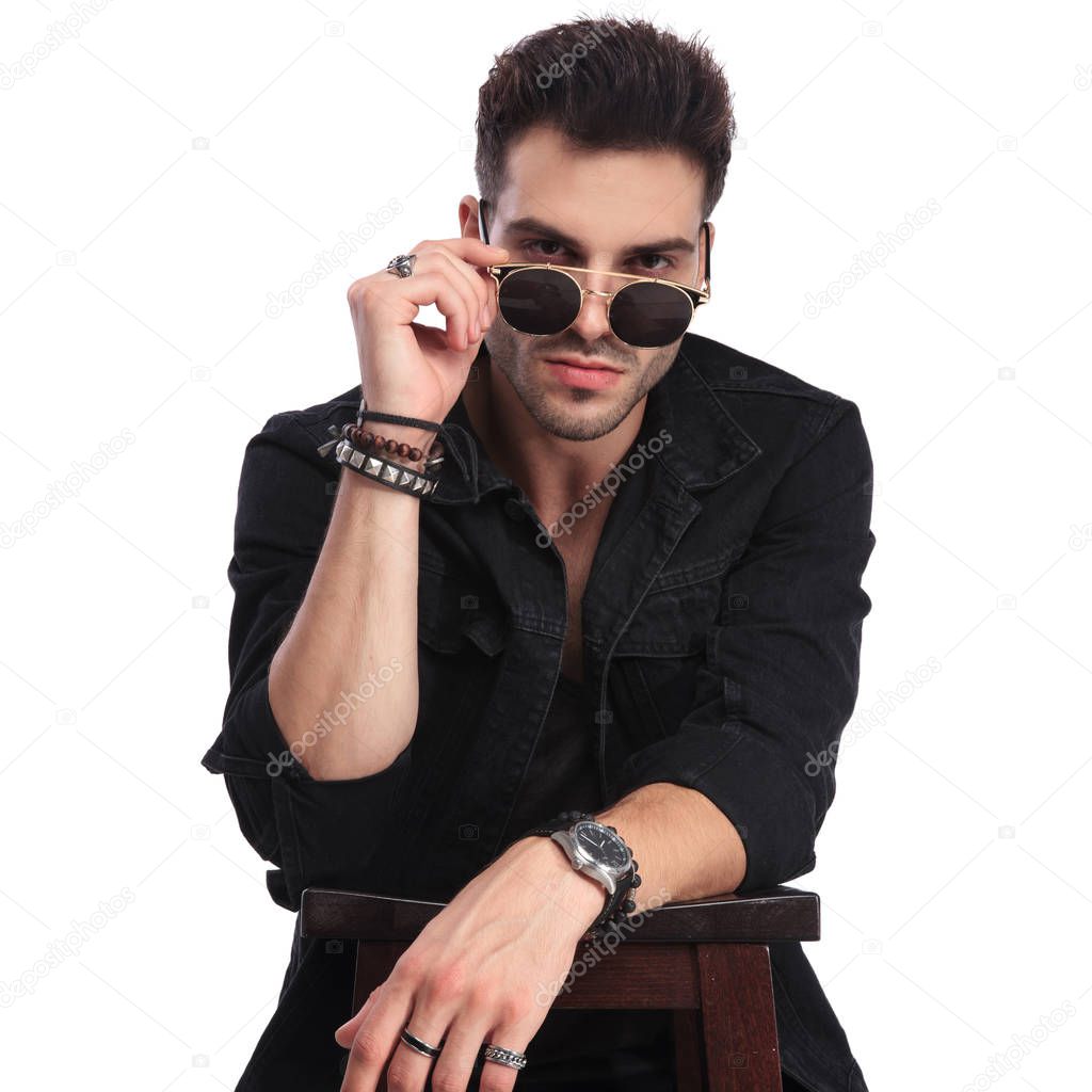 portrait of seductive man in black clothes standing in a bar at a table and looking over his sunglasses
