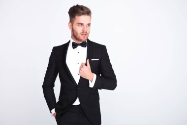 Yan ışık gri arka plan üzerinde dururken isteyen takım elbise yaka tutarak rahat adam portresi