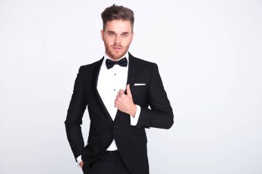 ışık gri arka plan üzerinde duran cep ve smokin yaka tutan genç adam portresi