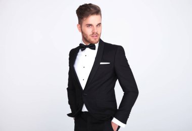 beyaz zemin üzerine siyah smokin ayakta çekici bir adam portresi ceplerinde eller