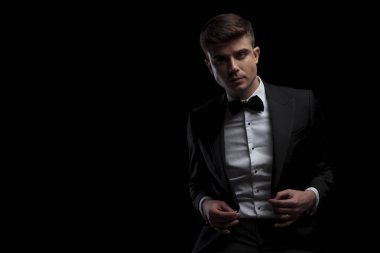 şık genç adam siyah arka plan üzerine oturur ve tarafa bakarken onun siyah takım düğmeleri