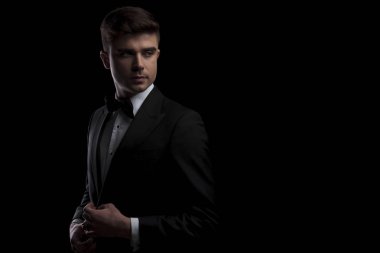 zarif adam onun siyah smokin düğmeler ve yan duran siyah arka plan üzerine görünüyor