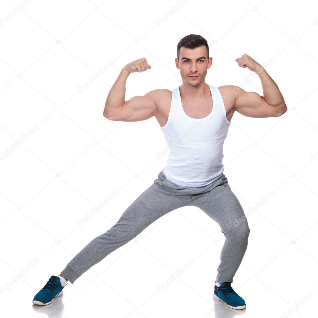 young fit man in undershirt training while standing on white background