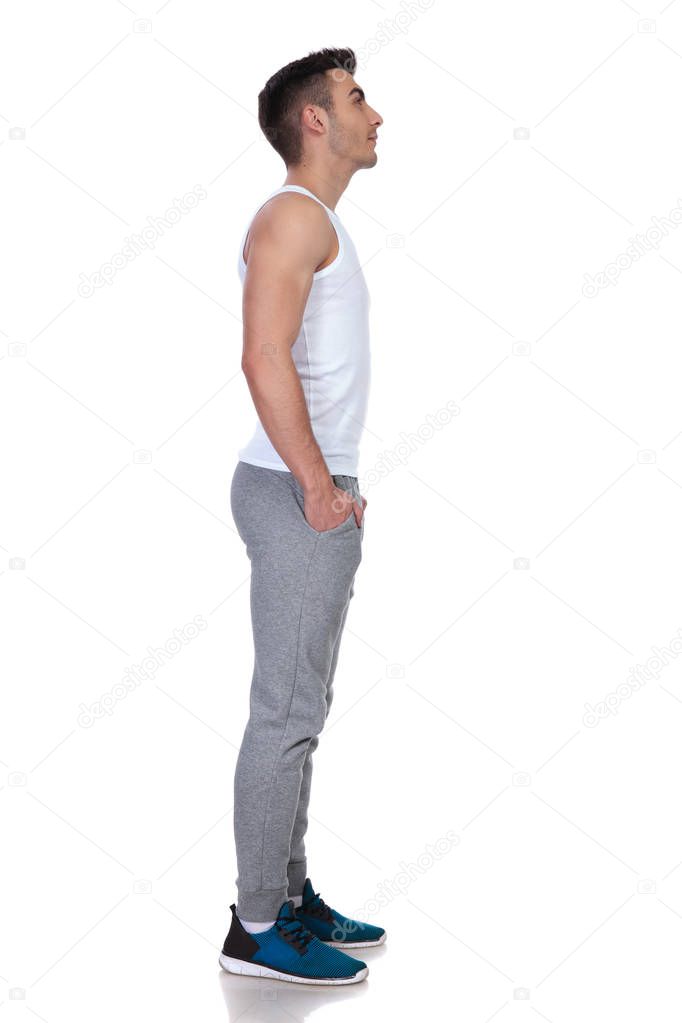 relaxed young man waiting in line looks up while standing on white background with hands in pockets