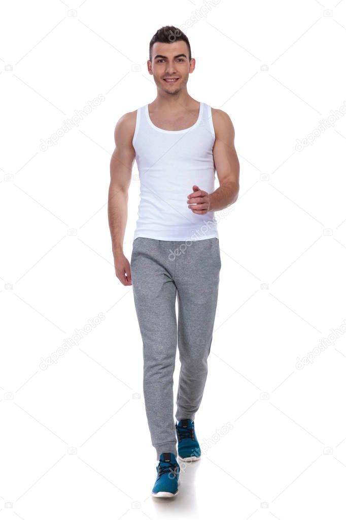smiling fitness man in white undershirt walking on white background, full body picture