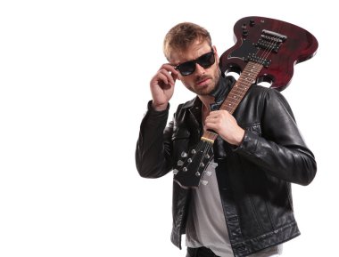 omuz düzeltmeleri güneş gözlüğü ve yan beyaz arka plan üzerinde dururken isteyen gitar ile yakışıklı rocker portresi