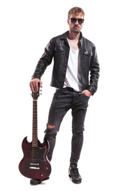 siyah deri ceket ve beyaz arka plan üzerinde dururken onun elektro gitar ile poz güneş gözlüğü giyiyor rahat moda adam