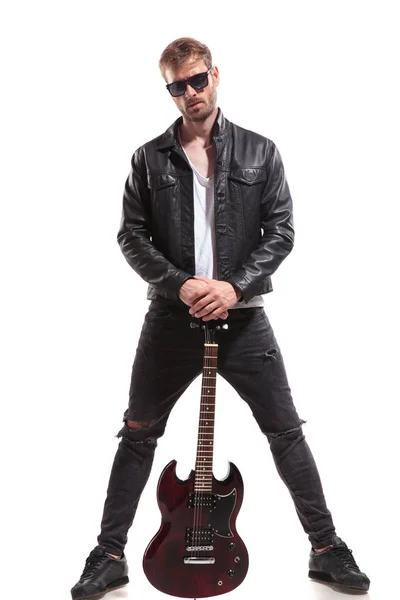 英俊的摇滚明星戴着太阳镜和皮革夹克摆在他的电吉他和站在白色背景 — 图库照片