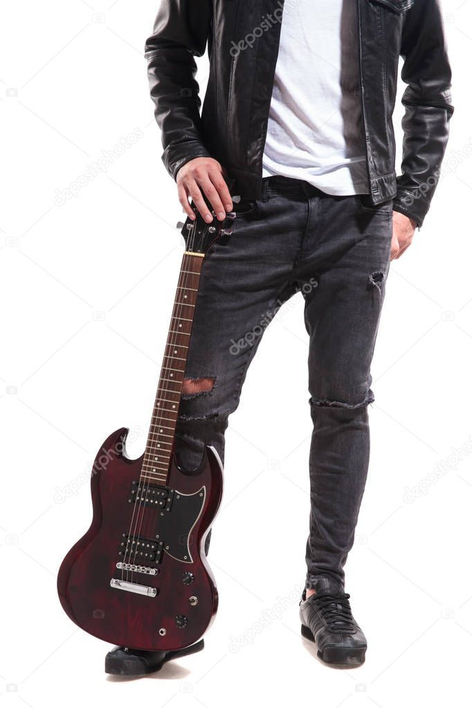 legs of rocker wearing ripped jeans and leather jacket holding his guitar on ground