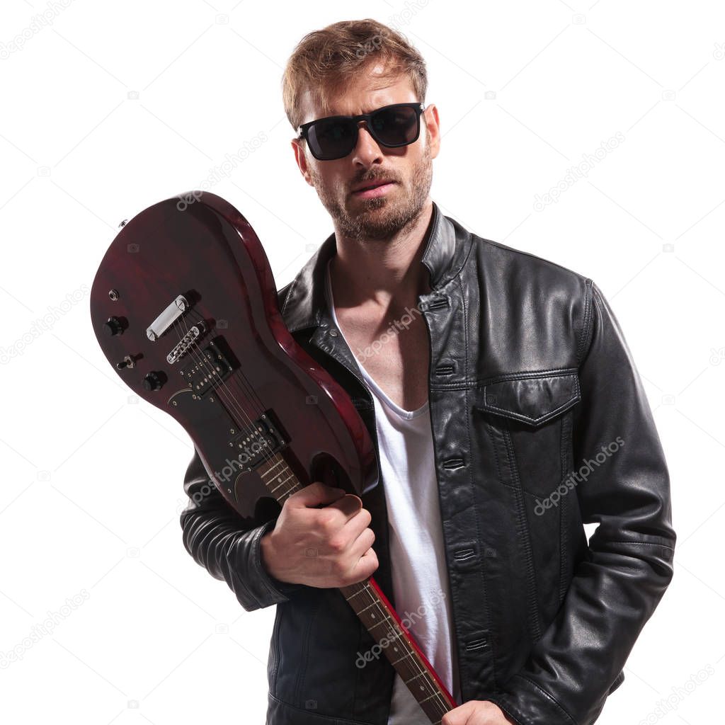 portrait of young rock star wearing sunglasses and leather jacket wanting to smash his electric guitar while standing on white background