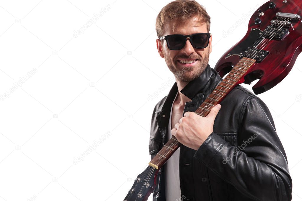 portrait of smiling man holding electric guitar on shoulder looking to side while standing on white background