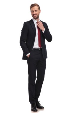 rahat işadamı kırmızı kravatını düzeltir ve yan duran beyaz arka plan üzerinde görünüyor