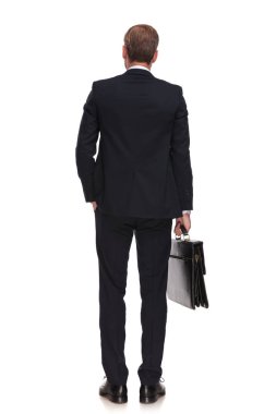 arkadan görünüşü rahat işadamı bir eli cebinde, tam uzunlukta resim ile beyaz arka plan üzerinde duran bir bavul holding