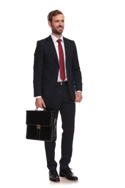 Beyaz arka plan üzerinde duran ve yan, tam vücut resme bakarak evrak çantası ile zarif işadamı