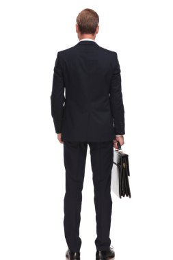 Arkadan bir evrak çantası tutarak ve cebinde el ile beyaz arka plan üzerinde duran rahat işadamı görünüşü