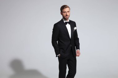 zarif delikanlı smokin ve papyon giyiyor elle gri arka plan üzerinde cebinde duruyor