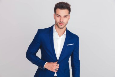 Mavi takımı ışık gri arka plan üzerinde dururken kadar düğmelerini genç akıllı casual adam portresi