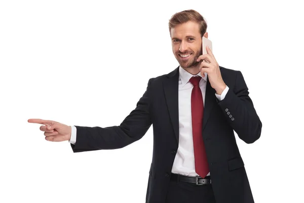 スーツと携帯電話で話していると 白い背景の上に立っている間側を指している赤いネクタイを身に着けている青年実業家の肖像画 — ストック写真