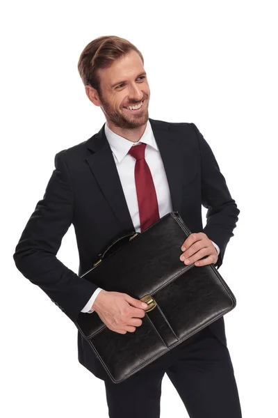 白い背景の上に立って 笑顔ながら側に黒のスーツケースを開くうれしそうなビジネスマンに見える — ストック写真