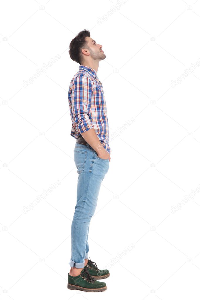 relaxed casual man waiting in line looks up at something while standing on white background with hands in pocets, full length picture