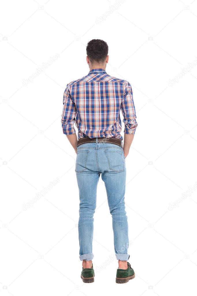 back view of relaxed man wearing shirt with blue checkers standing on white background with hands in pockets, full body picture