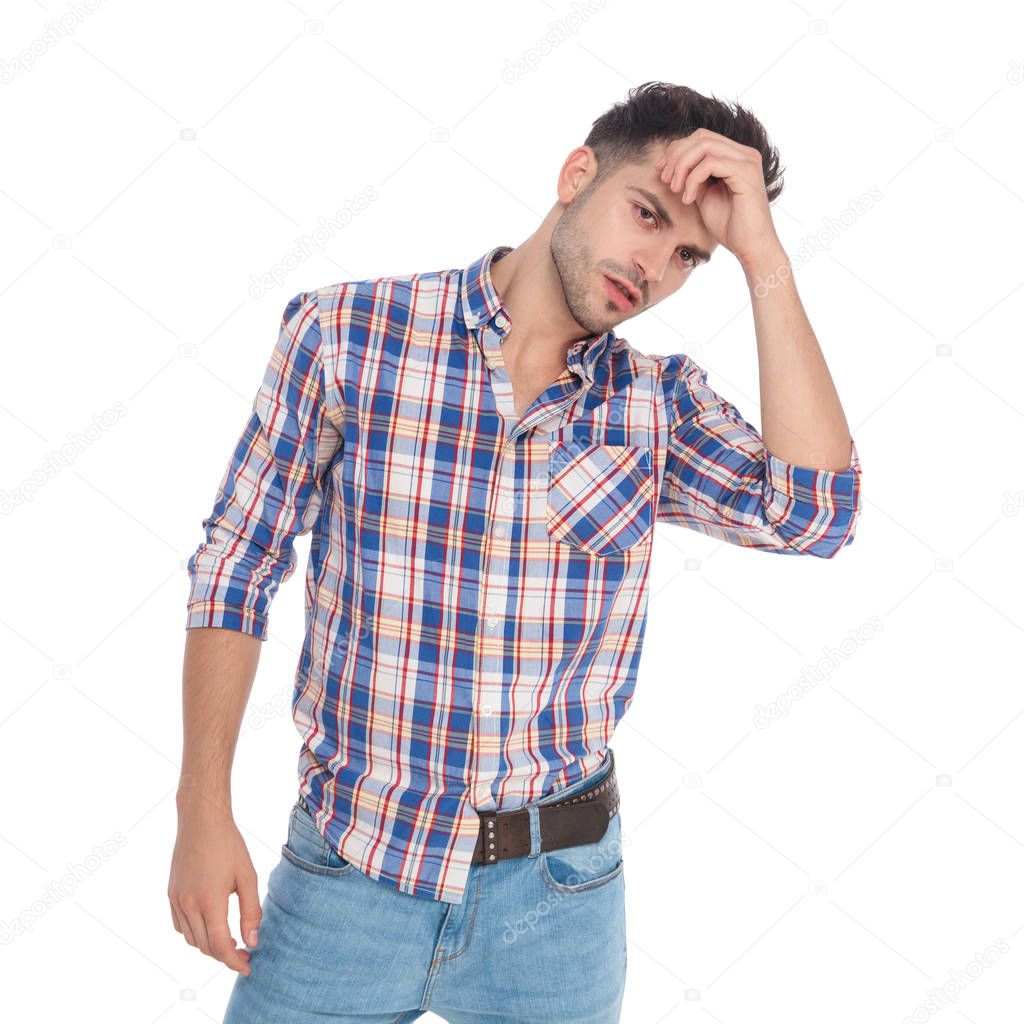 portrait of seductive casual man fixing his hair and looking to side while standing on white background