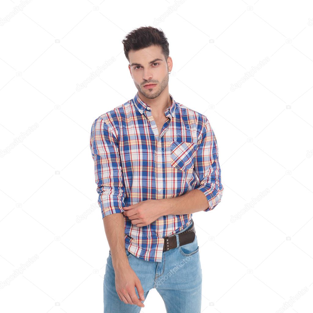 portrait of seductive man fixing his plaid shirt sleeve while standing on white background