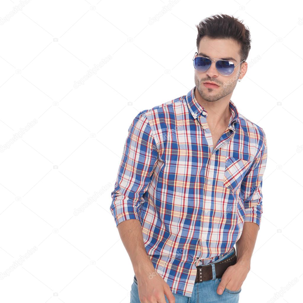 portrait of relaxed young man with sunglasses looks to side while standing on white background