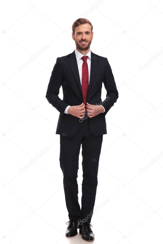 young and smiling businessman buttoning his suit while standing on white background