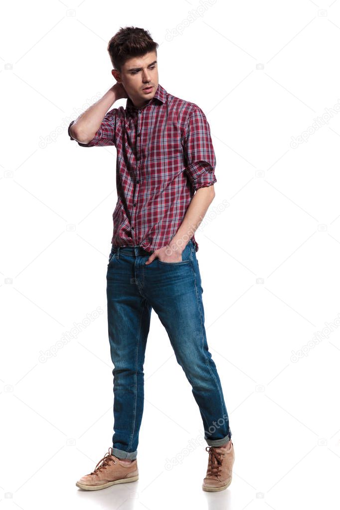 relaxed man holds head and looks down to side while stepping on white background, full body picture