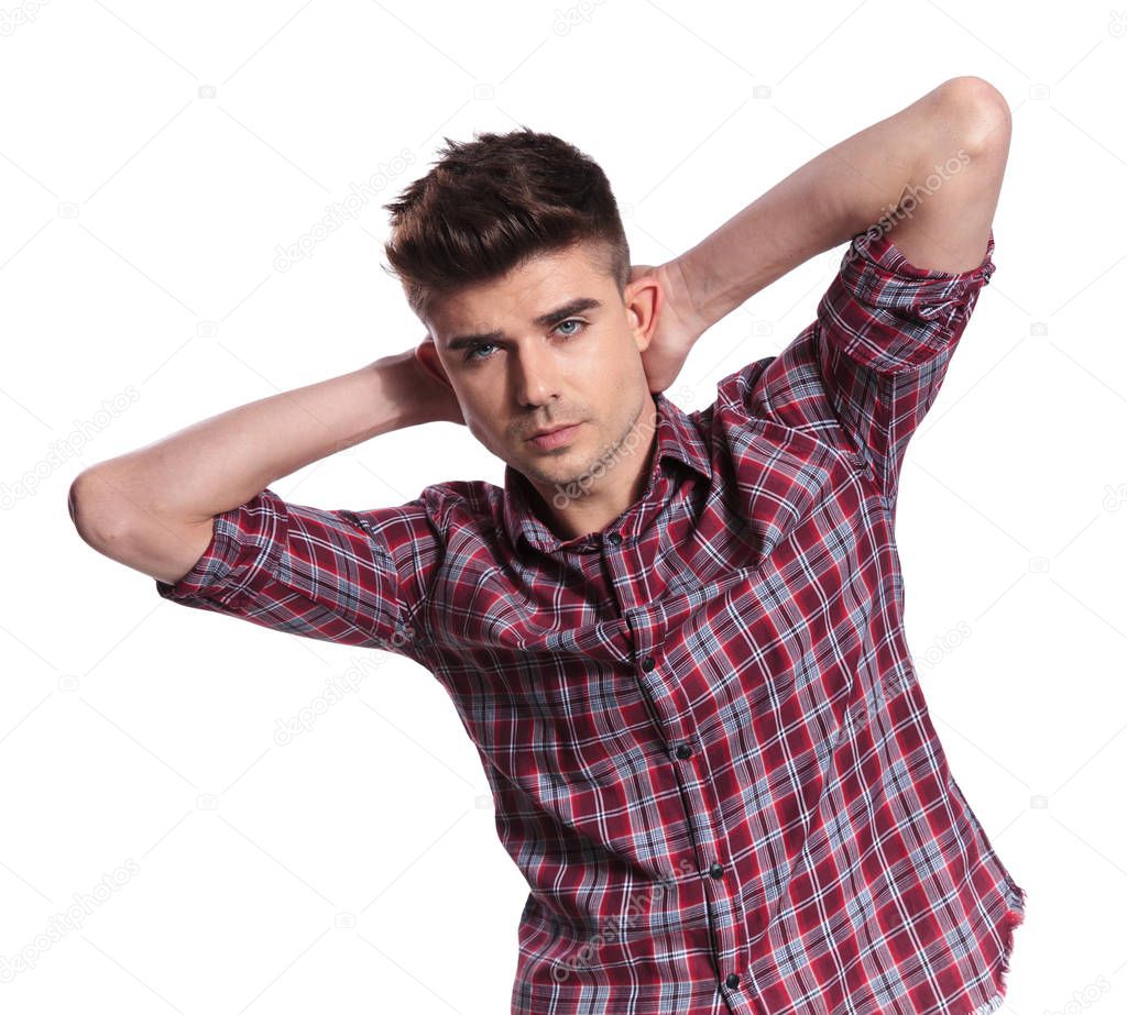 portrait of seductive young man wearing a shirt with checkers holding neck while standing on white background