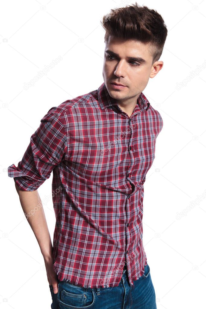 relaxed casual man wearing shirt with checkers looks to side while standing on white background with hands in back pockets, portrait picture