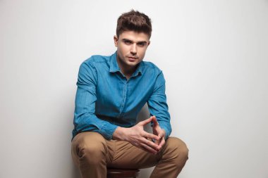gri bir duvar yakın ahşap bir sandalyede oturan ve avuç içi tutan çekici casual adam portre resim