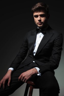 Smokin zarif genç adam gri arka plan üzerinde ahşap sandalye uyluk el dinlenme süre oturur