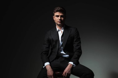 seksi damat portresi açık yaka ve geri alınan papyon gri arka plan üzerinde ahşap sandalye üzerinde oturan