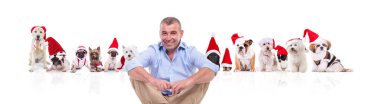 bacaklar ile oturan üst düzey casual adam santa kapaklar beyaz arka plan üzerinde giyen ve gülümseyerek birçok Noel köpekler önüne geçti