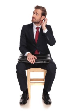 dalgın işadamı görüşme için bekleyen ve beyaz arka plan bir tahta sandalyede oturan ve kafa, tam uzunlukta resmini tutan tarafına bakar