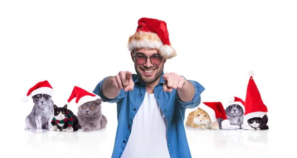 微笑的休闲男子的肖像在圣诞节猫的前面指向手指在白色背景上的圣诞老人 — 图库照片