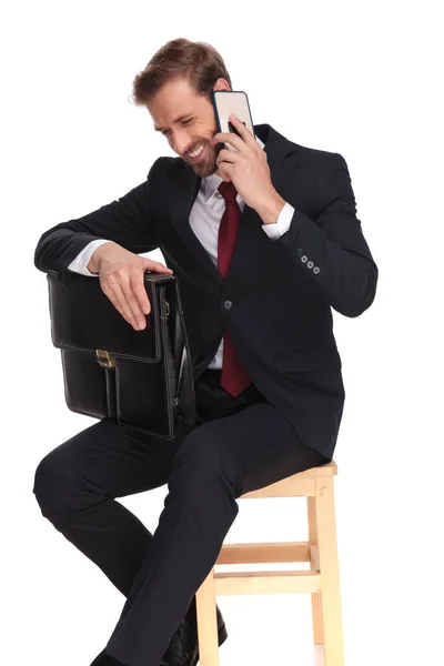 木製の椅子の上に座って 白い背景の上 電話で話しながら笑っているスーツケースと青年実業家 — ストック写真