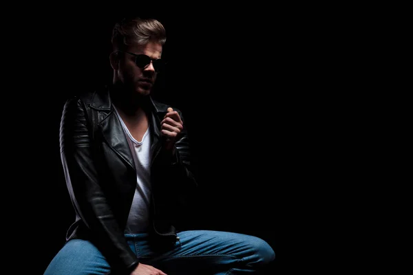 portrait of macho man in leather jacket holding chair and collar while sitting and looking down to side, portrait picture