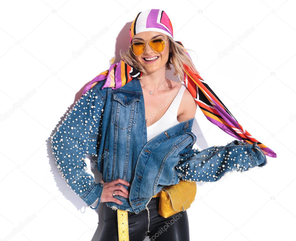 portrait of sexy blonde woman laughing while holding her colored headscarf and standing on white background with a hand on hip