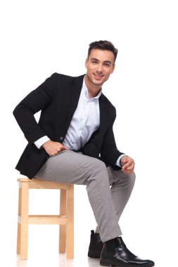 Beyaz arka plan üzerinde ahşap sandalye üzerinde oturan siyah elbiseli gülümseyen iş adamı yan görünüm